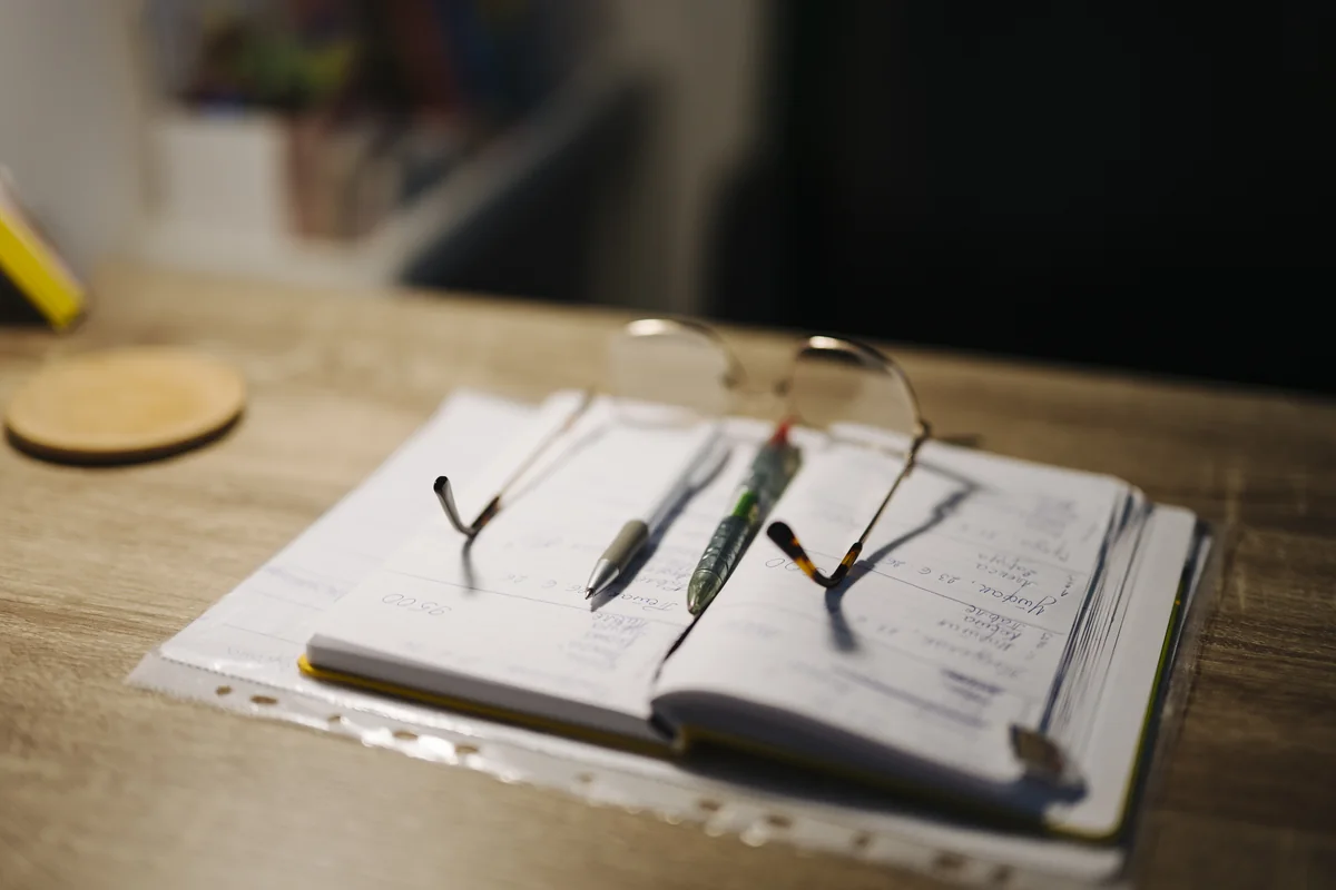 Illustrative notebook, pens and glasses on a desk for a private planning worksheet; not clinical evidence.